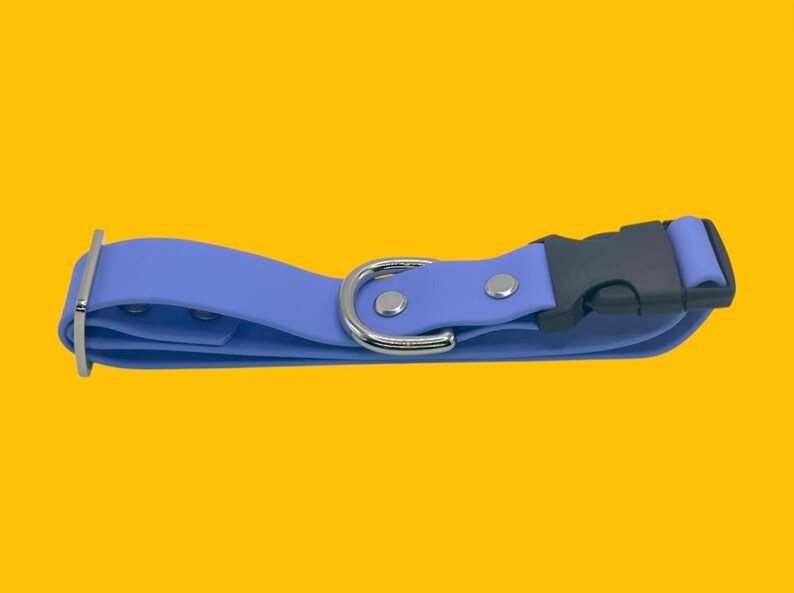 May include: A periwinkle blue dog collar with a black plastic buckle and a silver metal D-ring. The collar has a simple design with a metal slider and two silver rivets. The background is a solid yellow.