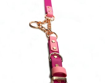 May include: A two-tone pink leather collar featuring rose gold-colored metal hardware, including a buckle, multiple D-rings, and a central chain link connector. The strap combines dark magenta and light pink sections secured with metal rivets.