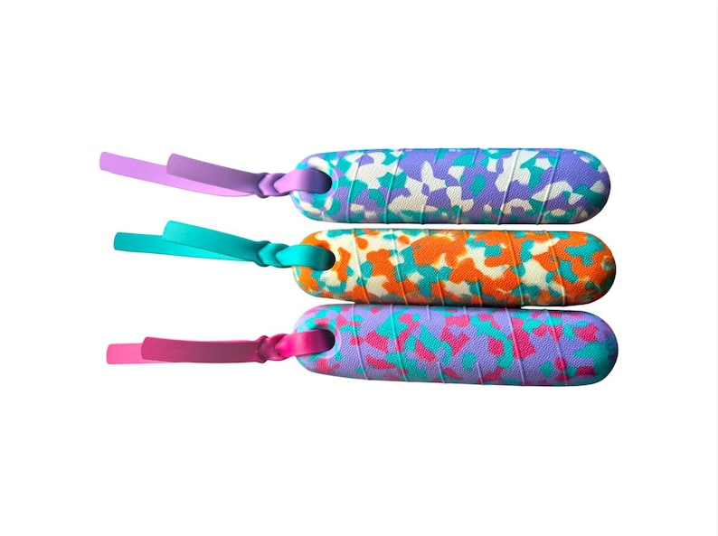 K&ouml;nnte beinhalten: Drei farbenfrohe Springseilgriffe mit Camouflage-Muster. Die Griffe sind in Lila-, T&uuml;rkis- und Oranget&ouml;nen gehalten. Jeder Griff hat eine farblich passende Schlaufe am Ende.