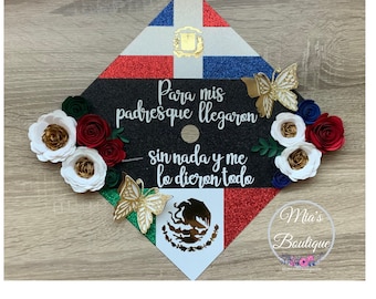 May include: Graduation cap decorated with the Dominican Republic and Mexican flags, gold butterflies, and paper flowers. The cap has the text "Para mis padres que llegaron sin nada y me lo dieron todo".