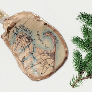 May include: An oyster shell Christmas ornament with a vintage map design, including the text "Jamestown Exposition". The shell is edged in gold and has a white and gold ribbon. A sprig of green pine adds a festive touch.
