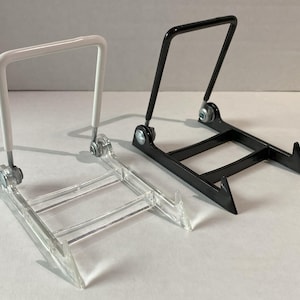 May include: Two display stands, one white and one black, are shown. The white stand has a clear base and a white, rectangular top. The black stand has a black base and a black, rectangular top. Both stands are made of metal and plastic.
