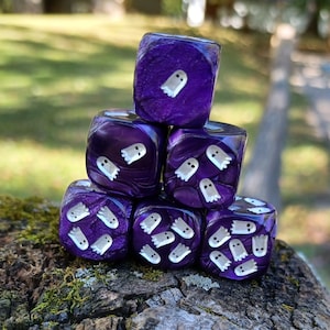May include: A stack of six purple dice with white ghost illustrations. The dice are arranged in a pyramid shape.