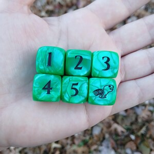 May include: Six green dice with white marbling are arranged in two rows. The dice are numbered 1 through 5, with the sixth die featuring a turtle graphic. The numbers and turtle are black.