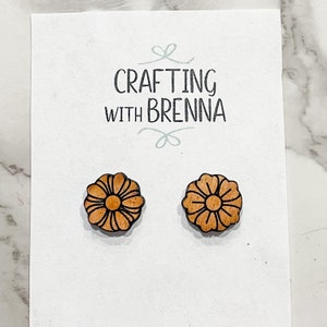 Puede incluir: Un par de pendientes de madera con forma de flor, con base de madera marr&oacute;n y contorno negro. Los pendientes se muestran en una tarjeta blanca con el texto "CRAFTING WITH BRENNA".