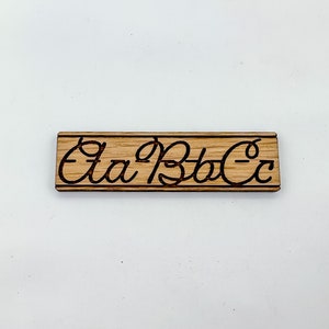 May include: A wooden sign with the cursive letters "Aa Bb Cc" burned into the surface.