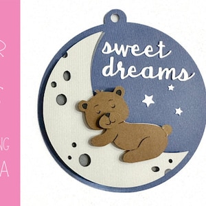 May include: A blue and white circle with a crescent moon and a brown bear sleeping on it. The text "sweet dreams" is written in white on the circle.