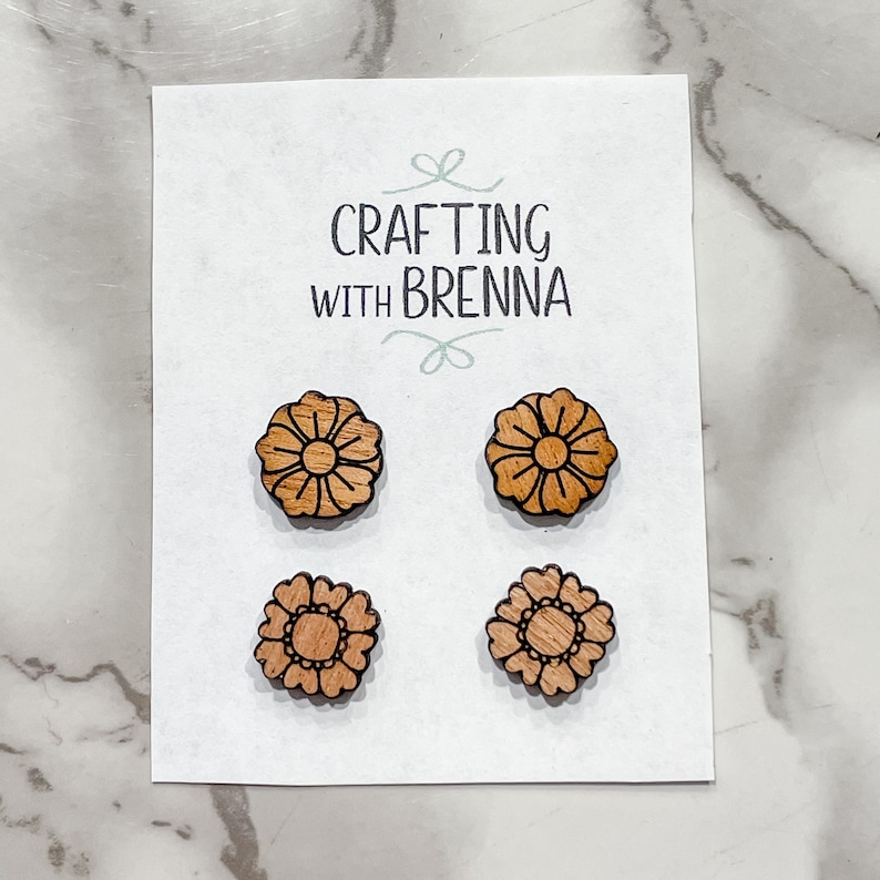 Puede incluir: Cuatro pendientes de madera en forma de flor en una tarjeta blanca con el texto "CRAFTING WITH BRENNA".
