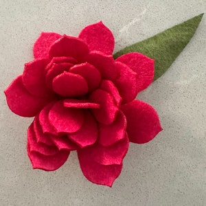 May include: A bright pink felt flower with a green felt leaf. The flower is made of many overlapping petals.