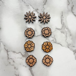 Puede incluir: Conjunto de seis pendientes de madera con forma de flor. Los pendientes son de dos estilos diferentes, uno con una forma simple de margarita y el otro con un dise&ntilde;o floral m&aacute;s intrincado. Los pendientes son todos de color marr&oacute;n claro.