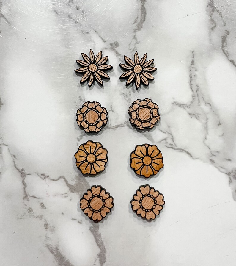 Puede incluir: Conjunto de seis pendientes de madera con forma de flor. Los pendientes son de dos estilos diferentes, uno con una forma simple de margarita y el otro con un dise&ntilde;o floral m&aacute;s intrincado. Los pendientes son todos de color marr&oacute;n claro.