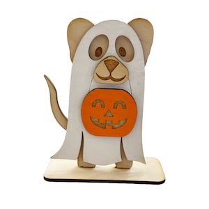 Puede incluir: Una decoración de Halloween de madera de un perro vestido de fantasma sosteniendo una calabaza.