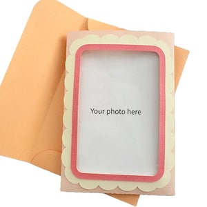 Pode incluir: Um cartão de felicitações com uma borda ondulada e uma abertura retangular, emoldurada em rosa. O cartão diz "Your photo here" e é acompanhado por um envelope cor de pêssego.