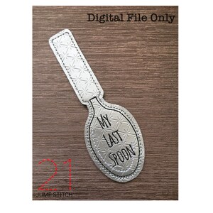 May include: A silver spoon with the text "My Last Spoon" embroidered on it. The spoon is on a wood background.