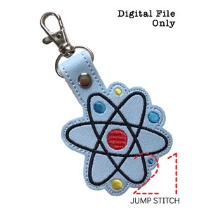 May include: A light blue leather keychain with an embroidered atom design. The atom is black with red, blue, and yellow accents. The keychain has a silver jump ring and a silver split ring.