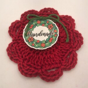 May include: Red crocheted coaster with a green ribbon and a round tag that says "Handmade" with a Christmas wreath design.