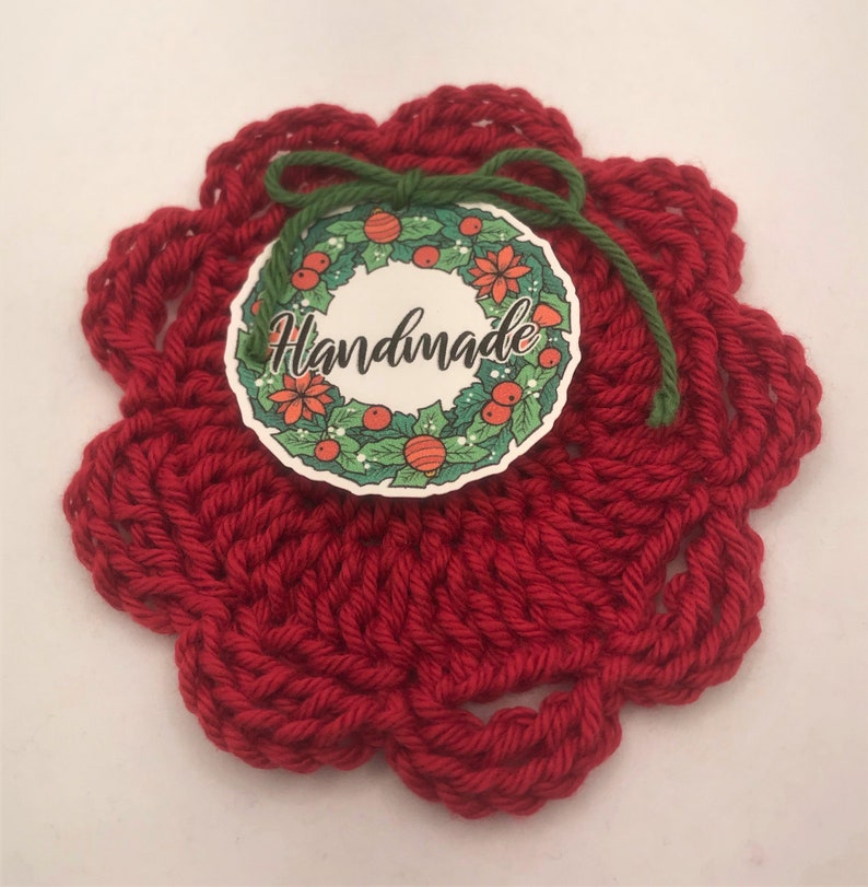 May include: Red crocheted coaster with a green ribbon and a round tag that says "Handmade" with a Christmas wreath design.