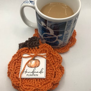 May include: Two crocheted pumpkin-shaped coasters. The coaster on top has a tag that says "Handmade Pumpkin".