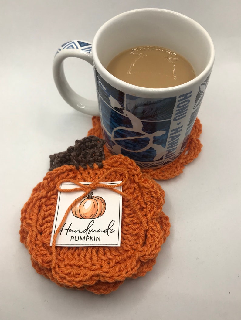 May include: Two crocheted pumpkin-shaped coasters. The coaster on top has a tag that says "Handmade Pumpkin".
