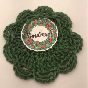 May include: Green crocheted coaster with a round, white tag that says "Handmade" and features a red and green Christmas wreath design.