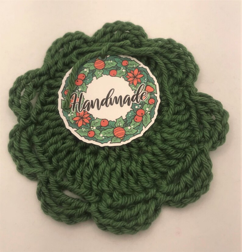 May include: Green crocheted coaster with a round, white tag that says "Handmade" and features a red and green Christmas wreath design.