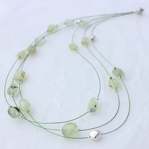 May include: A multi-strand necklace featuring green gemstone beads and silver accents. The necklace is crafted from thin, green wire.