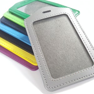 May include: A stack of colorful leather ID badge holders with a clear plastic window for displaying identification cards. The holders are stitched with a decorative stitch around the edges.