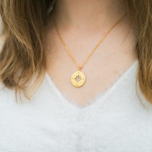 May include: A gold necklace with a compass pendant featuring a star design and the letters N, W, E, and S.