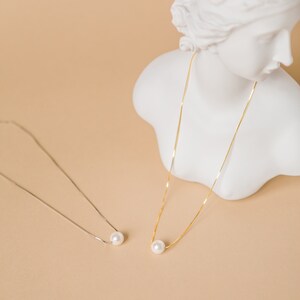 May include: Two delicate necklaces with single pearl pendants. One necklace is gold and the other is silver. Both necklaces are displayed on a white bust.