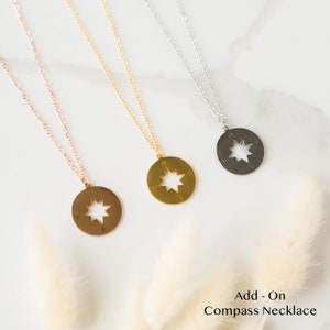 Op de afbeelding: Drie gouden, ros&eacute;gouden en zilveren kettingen met kompas hangers. Elke hanger heeft een stervormige uitsparing en de letters N, S, E en W rond de rand. Kompas ketting als accessoire.
