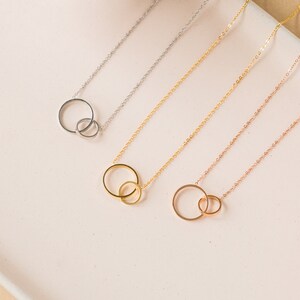 May include: Four necklaces with interlocking circle pendants. The necklaces are silver, gold, rose gold, and a combination of gold and rose gold.