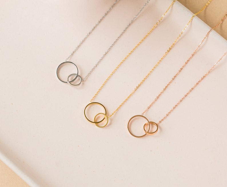 May include: Four necklaces with interlocking circle pendants. The necklaces are silver, gold, rose gold, and a combination of gold and rose gold.