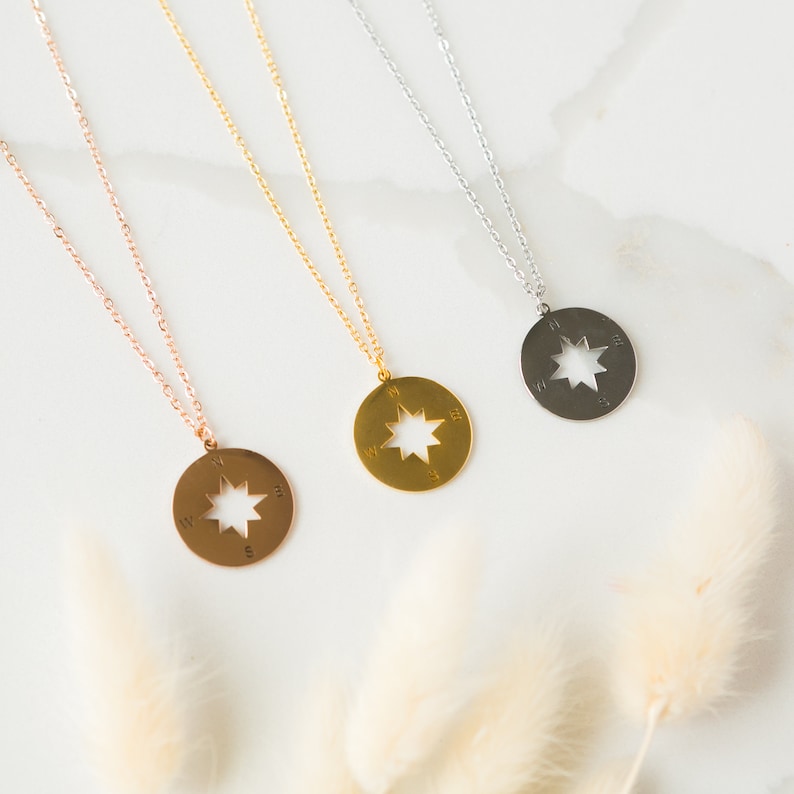 May include: Three gold, silver, and rose gold necklaces with compass pendants. Each pendant features a star design with compass directions.