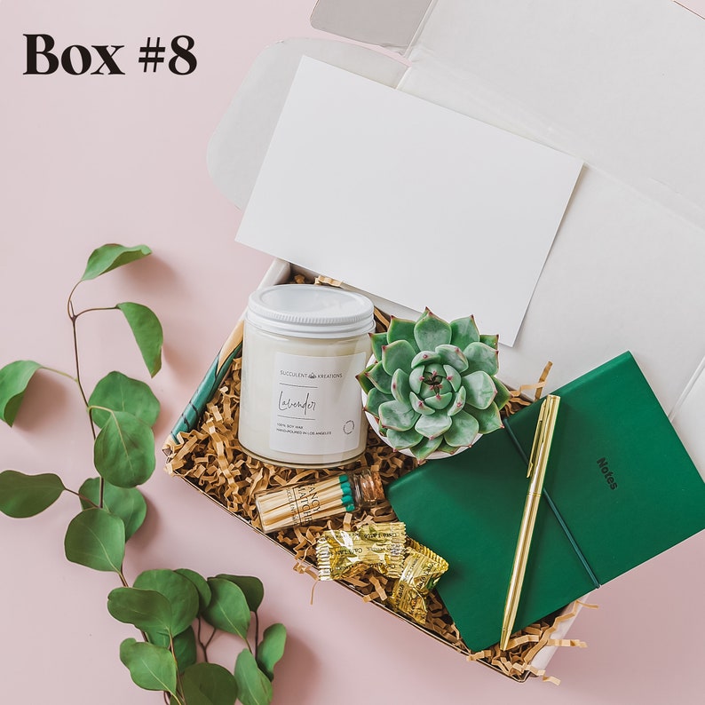 May include: A green gift box filled with a white candle, a small succulent plant, a green notebook, a gold pen, and matches. The candle label reads "Excellent Creations Lavender".