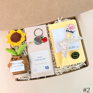 May include: A gift box with a crocheted sunflower and a small pot with the text "Thank You For Helping Me Grow". Includes a bar of milk chocolate, a keychain with an apple charm, and a yellow notebook with a pencil and a ribbon.