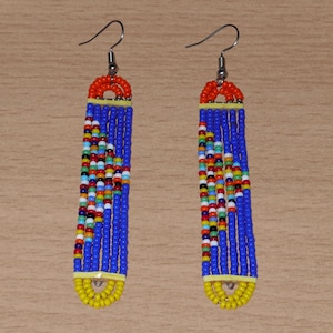Op de afbeelding: Een paar lange, kralen oorbellen met een blauw, geel, oranje en veelkleurig ontwerp.