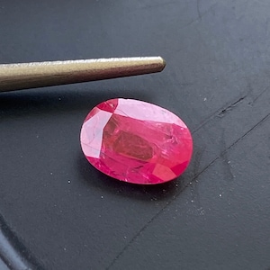 May include: A vibrant pink oval-shaped gemstone with a smooth, polished surface.