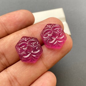 Op de afbeelding: Twee roze gegraveerde edelsteen cabochons met een zeshoekige vorm en ingewikkelde bloemmotieven.