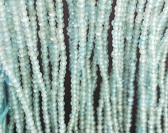 May include: A close-up of multiple strands of light blue aquamarine beads. The beads are faceted and have a smooth, polished finish.