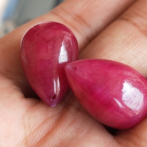 Op de afbeelding: Twee traanvormige robijnrode edelstenen met een gladde, gepolijste afwerking.