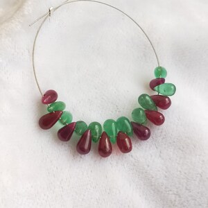 Op de afbeelding: Een zilveren oorring met een druppelvormig smaragd- en robijn-edelsteendesign. De edelstenen zijn in een cascade-patroon gerangschikt.