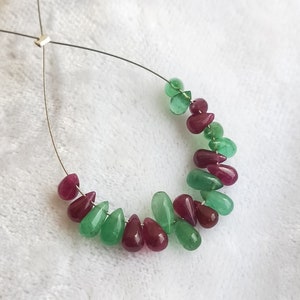 May include: A strand of teardrop-shaped beads in shades of green and red. The beads are strung on a silver wire.