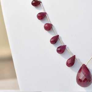 May include: A necklace made with a silver chain and teardrop-shaped ruby beads.