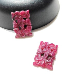 Puede incluir: Dos colgantes tallados de piedra preciosa de color rubí rojo con diseños florales.