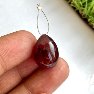 May include: A teardrop-shaped pendant made of a deep red gemstone with a silver loop and a gold bead at the top.