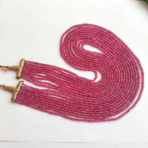 Puede incluir: Una larga hebra de cuentas de piedras preciosas rosadas con cierres dorados. Las cuentas son pequeñas y facetadas, creando un efecto brillante.
