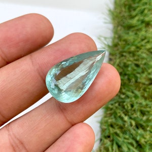 May include: A teardrop-shaped aquamarine gemstone with a light blue color and a faceted cut.