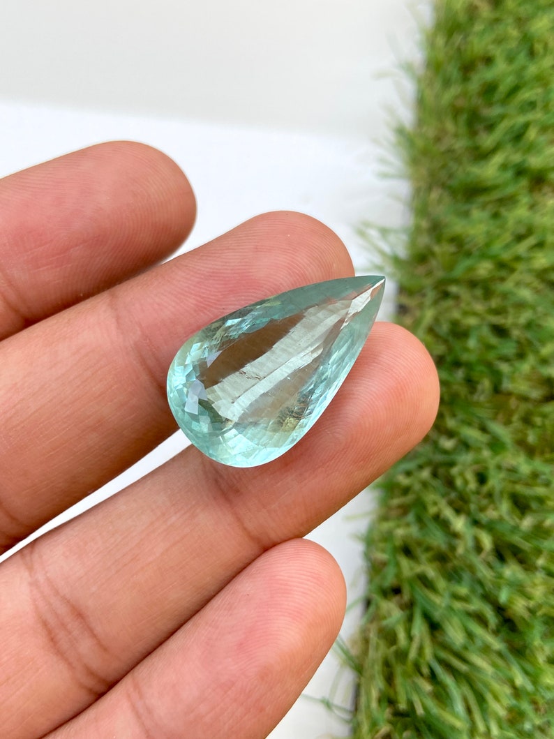 May include: A teardrop-shaped aquamarine gemstone with a light blue color and a faceted cut.