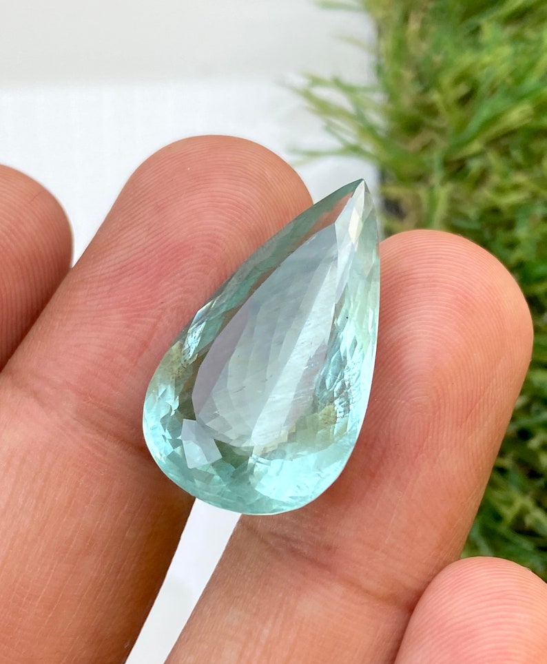 May include: A teardrop-shaped aquamarine gemstone with a light blue color and a faceted cut.