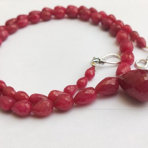 May include: A red gemstone necklace with a teardrop-shaped pendant. The necklace is made of faceted beads and has a silver clasp.